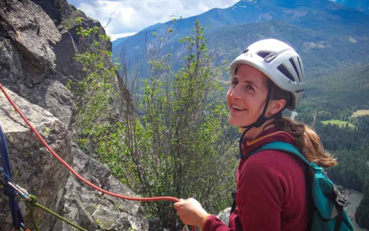 a person smiles as they hold a rope while rock climbing